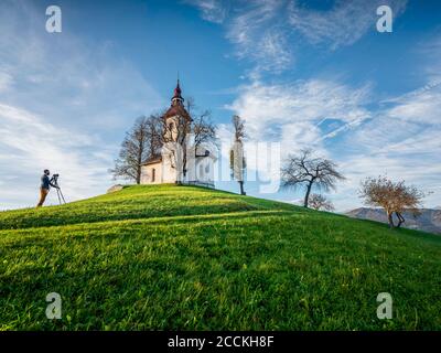 Slovénie, haute-Carniola, municipalité de Skofja Loka, Homme photographiant l'église Saint-Thomass en automne Banque D'Images