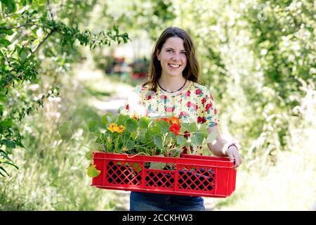 Jeune femme souriante portant du nasturtium dans un panier à la ferme Banque D'Images