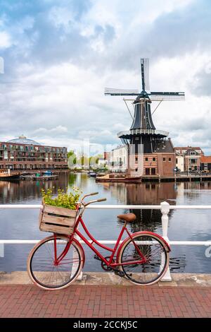 Pays-Bas, Hollande-Nord, Haarlem, vélo stationné le long de la rampe du pont du canal avec moulin à vent de Adriaan en arrière-plan Banque D'Images