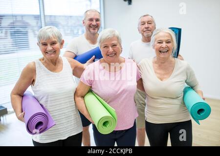 Groupe d'aînés heureux tenant des tapis pour les cours de yoga Banque D'Images