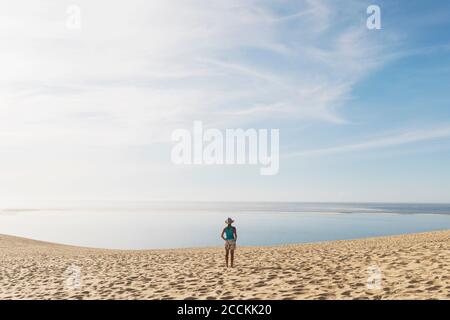 Femme regardant l'océan Atlantique en se tenant sur la plage pendant la journée ensoleillée, Dune de Pilat, Nouvelle-Aquitaine, France Banque D'Images