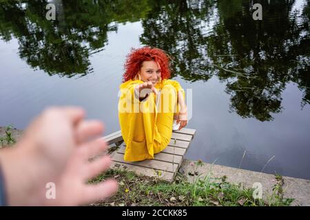 Jeune femme avec des cheveux bouclés et un costume jaune assis au bord de la rivière , atteignant la main de l'homme Banque D'Images