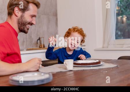 Père et fils heureux regardant le gâteau au chocolat au dîner table dans la cuisine Banque D'Images