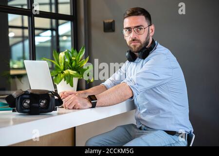 Beau homme d'affaires assis avec un casque et un ordinateur portable au bureau bureau de travail créatif Banque D'Images