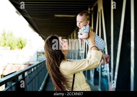 Mère levant son bébé garçon sur un pont Banque D'Images
