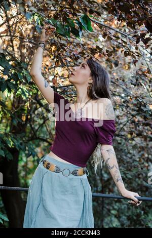 Portrait d'une jeune femme touchant les feuilles d'arbre dans le parc Banque D'Images