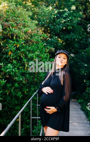 Femme enceinte qui se fait pister en se tenant sur la passerelle contre les arbres stationnement Banque D'Images