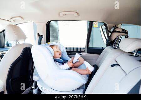 Bébé garçon assis dans le siège d'enfant et regardant dans le miroir dans une voiture Banque D'Images