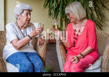 Des amies séniors toaster des flûtes à champagne tout en étant assis sur des chaises sur le patio Banque D'Images