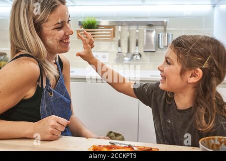 Une fille ludique qui se tache le nez de la mère avec de la sauce dans la cuisine Banque D'Images