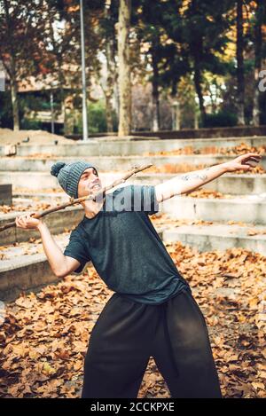 Homme souriant en tricot chapeau jeter bâton dans le parc pendant automne Banque D'Images