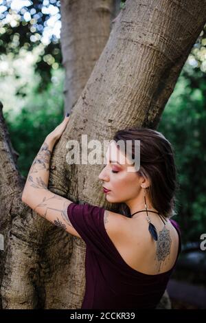 Portrait of young woman hugging tree in park Banque D'Images