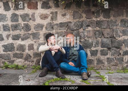 Couple gay parlant en étant assis sur le sentier contre le mur de pierre Banque D'Images