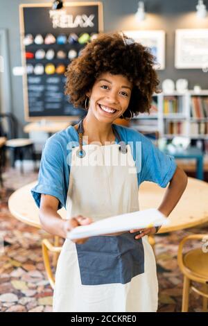 Bonne femme propriétaire qui tient le menu tout en se tenant à la main branché au café-restaurant Banque D'Images