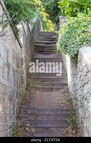 De vieux marches en pierre menant à un passage étroit avec de hauts murs de pierre dans un village anglais en été. Banque D'Images