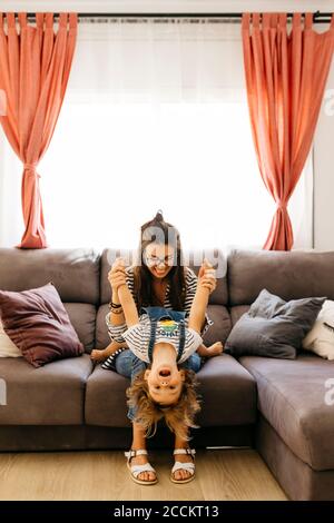 Mère tenant les mains de sa fille joueuse tout en étant assise avec elle canapé à la maison Banque D'Images