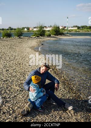 Le père et la fille parlent tout en étant assis sur une bûche à la rive contre le ciel pendant la journée ensoleillée Banque D'Images