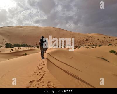 Vue arrière de deux touristes marchant sur une dune de sable Dans le désert de Merzouga Banque D'Images