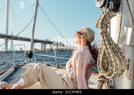 Vue latérale d'une femme mûre assise sur un yacht et profitant de la journée ensoleillée. Femme sénior se détendant sur un bateau privé. Banque D'Images