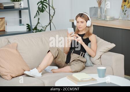 Jolie jeune femme dans des écouteurs et vêtements décontractés regarder des vidéos en ligne Banque D'Images