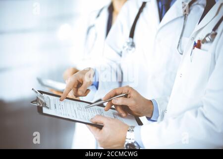 Des médecins inconnus, deux hommes et une femme, discutent des examens médicaux, tout en se tenant au bureau de l'hôpital. Médecins utilisant des planches à découper pour remplir Banque D'Images