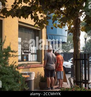 Hivers, Californie, États-Unis, 23 août 2020. Les clients portant des revêtements de visage en ligne devant le café Putah Creek pour le petit-déjeuner à emporter lisent le menu et les règles du magasin Banque D'Images