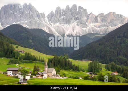 Vue emblématique d'une vallée du nord de l'Italie, avec une petite église entourée de prairies et d'arbres au premier plan et une chaîne de montagnes en arrière-plan Banque D'Images