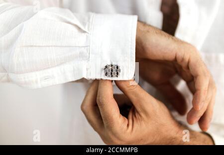 Mains blanches de sexe masculin plaçant des boutons de manchette sur les manches de son chemise blanche Banque D'Images