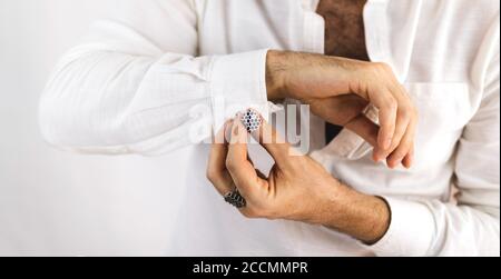 Mains blanches de sexe masculin plaçant des boutons de manchette sur les manches de sa chemise blanche. Banque D'Images