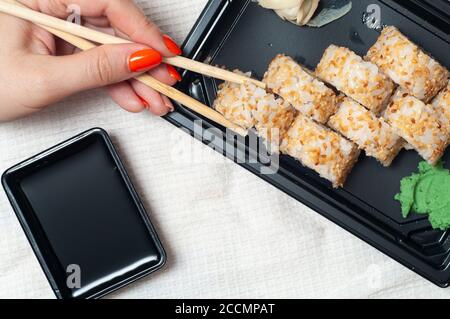 Femme mangeant des sushis livrés à la maison à partir d'un contenant avec des bâtons japonais. Vue de dessus Banque D'Images