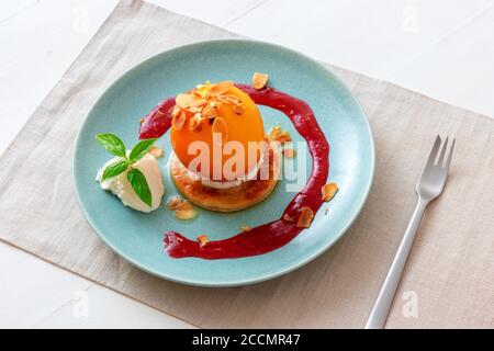 Pêches rôties avec crème fraîche au citron, citron vert et basilic et coulis de framboises. Délicieux dessert aux fruits doux, le Gordon Ramsey. Fond de table en bois blanc Banque D'Images