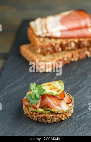 Griller du pain de seigle avec du jamon (prosciutto) et de la courgette frite sur une assiette en ardoise noire. En-cas gastronomique. Mise au point sélective Banque D'Images