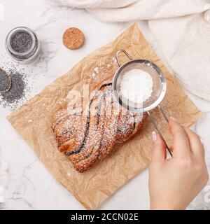 Tarte tressée (en osier) maison avec remplissage de graines de pavot. La femme décorera le gâteau avec du sucre en poudre. Pâtisseries fraîches pour le thé et le café. Sél Banque D'Images