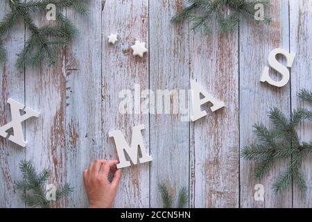 Plateau de Noël créatif sur des planches de bois rustiques. Tenez la lettre M dans le mot Noël. Brindilles de sapin décorées de flocons de neige en bois et de trinke aux étoiles blanches Banque D'Images