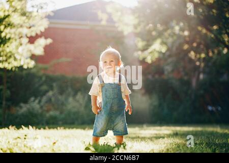 Joli petit garçon debout dans le parc à l'extérieur au coucher du soleil. Adorable enfant souriant un enfant d'un an qui marche à l'extérieur sur l'arrière-cour. Drôle d'enfant. Le plus authentique de la vie Banque D'Images