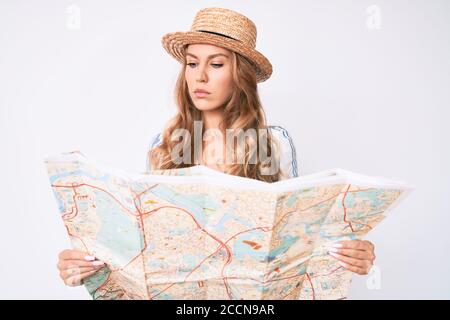 Jeune femme caucasienne aux cheveux blonds portant un chapeau d'été tenant la carte détendue avec une expression sérieuse sur le visage. Simple et naturel regardant la caméra Banque D'Images