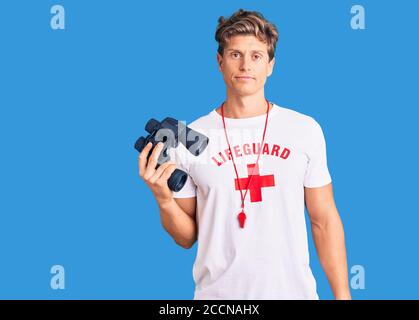 Jeune homme beau portant un t-shirt de maître-nageur utilisant des jumelles pensant l'attitude et une expression sobre qui a l'air confiante Banque D'Images