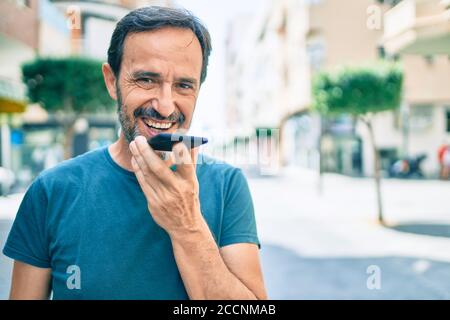 Homme d'âge moyen avec barbe souriante plein air envoi de la voix message sur le téléphone Banque D'Images