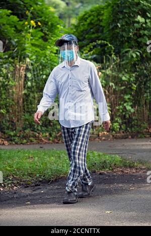 Un homme américain asiatique portant à la fois un masque chirurgical et un masque facial marche à Kissena Park à Flushing, Queens, New York City. Banque D'Images