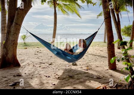 Plage hamac. Homme se détendant dans un hamac accroché entre les arbres sur une plage tropicale contre le soleil couchant. Thaïlande Asie du Sud-est Banque D'Images