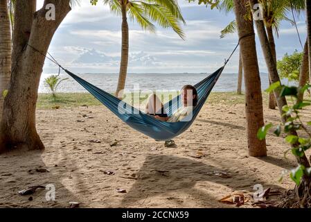 Plage hamac. Homme se détendant dans un hamac accroché entre les arbres sur une plage tropicale contre le soleil couchant. Thaïlande Asie du Sud-est Banque D'Images