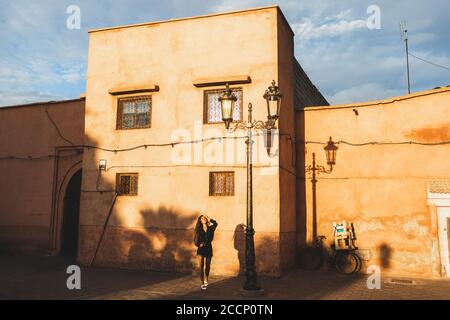 Jeune belle femme marchant dans la rue de Marrakech. Ville rouge, arrière-plan de couleur terre cuite. Lumière du coucher du soleil. Mode de vie. Banque D'Images