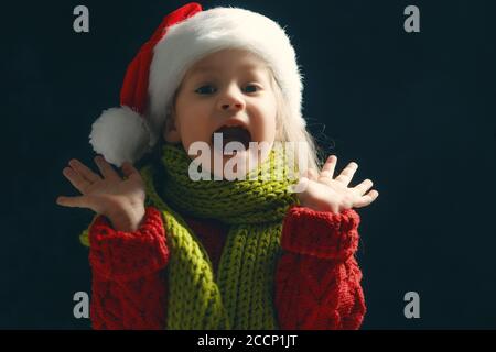 Joyeux enfant fille dans chapeau de père Noël sur fond sombre. Petit enfant émerveillé à Noël. Banque D'Images