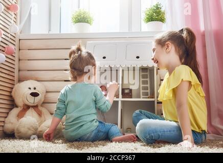 Les filles de sœurs heureuses jouent avec la maison de poupée à la maison. Les enfants adorables et drôles s'amusent dans la chambre des enfants. Banque D'Images