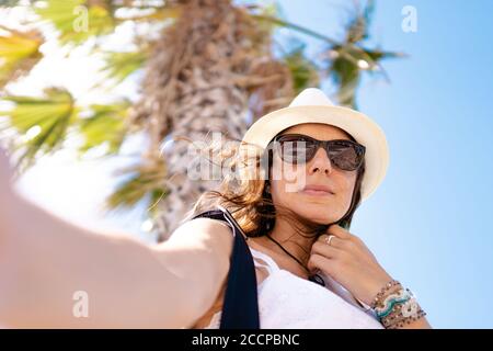 Touriste caucasien avec lunettes de soleil et chapeau blanc prenant selfie En vacances tropicales - femme connectée touriste avec smartphone prendre un auto-portra Banque D'Images