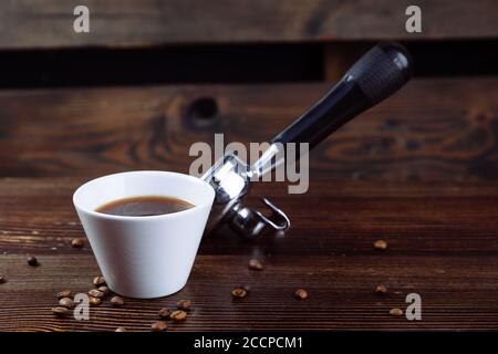 Une tasse de café noir, de grains de café torréfiés et un porte-machine à espresso sur fond sombre. Banque D'Images