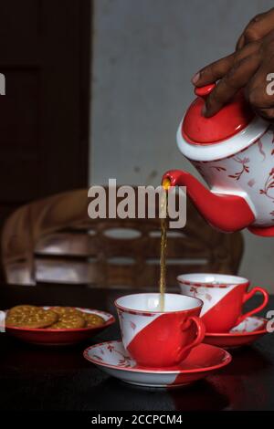 Verser le thé dans une tasse en céramique sur une table en bois avec un biscuit sur la plaque. Mise au point partielle. Banque D'Images