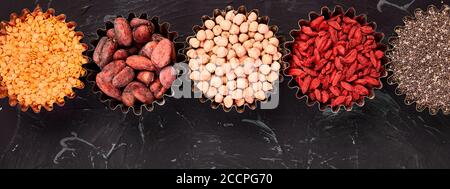 Bannière de plusieurs superaliments dans un petit bol sur fond noir. Superalimentation comme le chia, le cacao cru, le goji, les pois chiches, les lentilles. Copier l'espace. Pose à plat. Banque D'Images