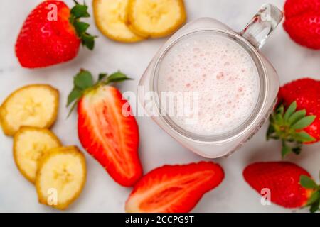 Smoothie ou cocktail milkshake à base de fraises fraîches, banane, yaourt ou lait et glaçons dans un pot Mason placé sur une table en marbre. Concept de santé v Banque D'Images