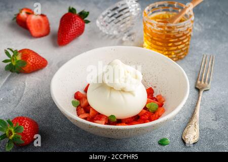 Fromage burrata gastronomique avec tartare de fraise à la menthe et au miel dans une assiette légère sur fond de béton gris ou de pierre. Petit déjeuner. Un appet délicieux Banque D'Images